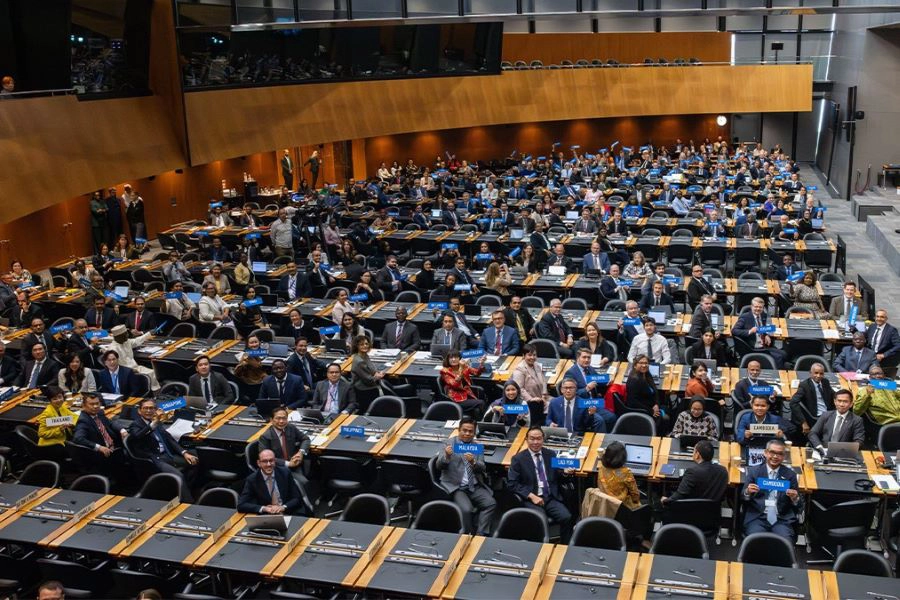 Crowd of delegates at WTO assembly seated on desk-chairs